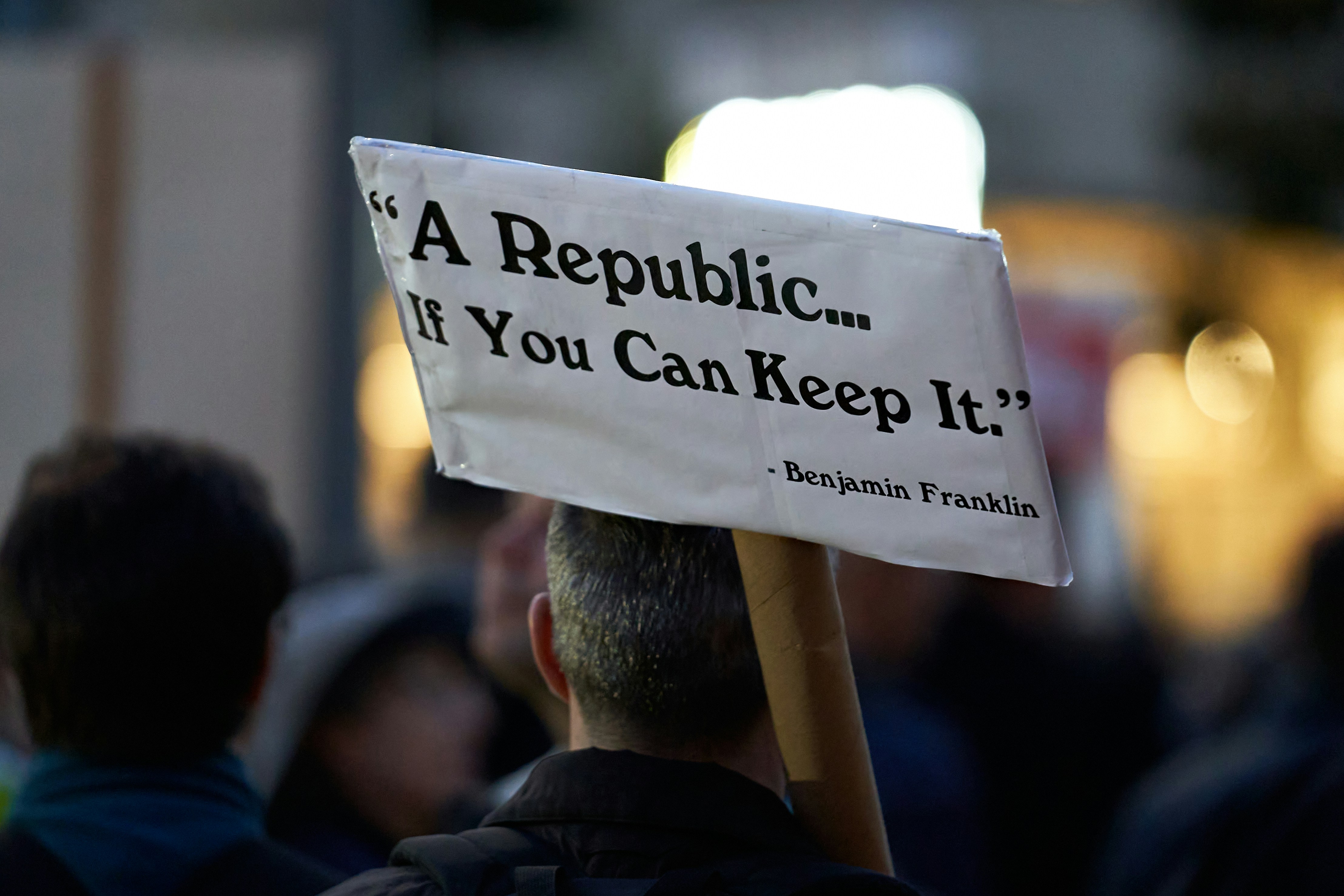 A protester holds a sign reading "A Republic... If You Can Keep It. - Benjamin Franklin".